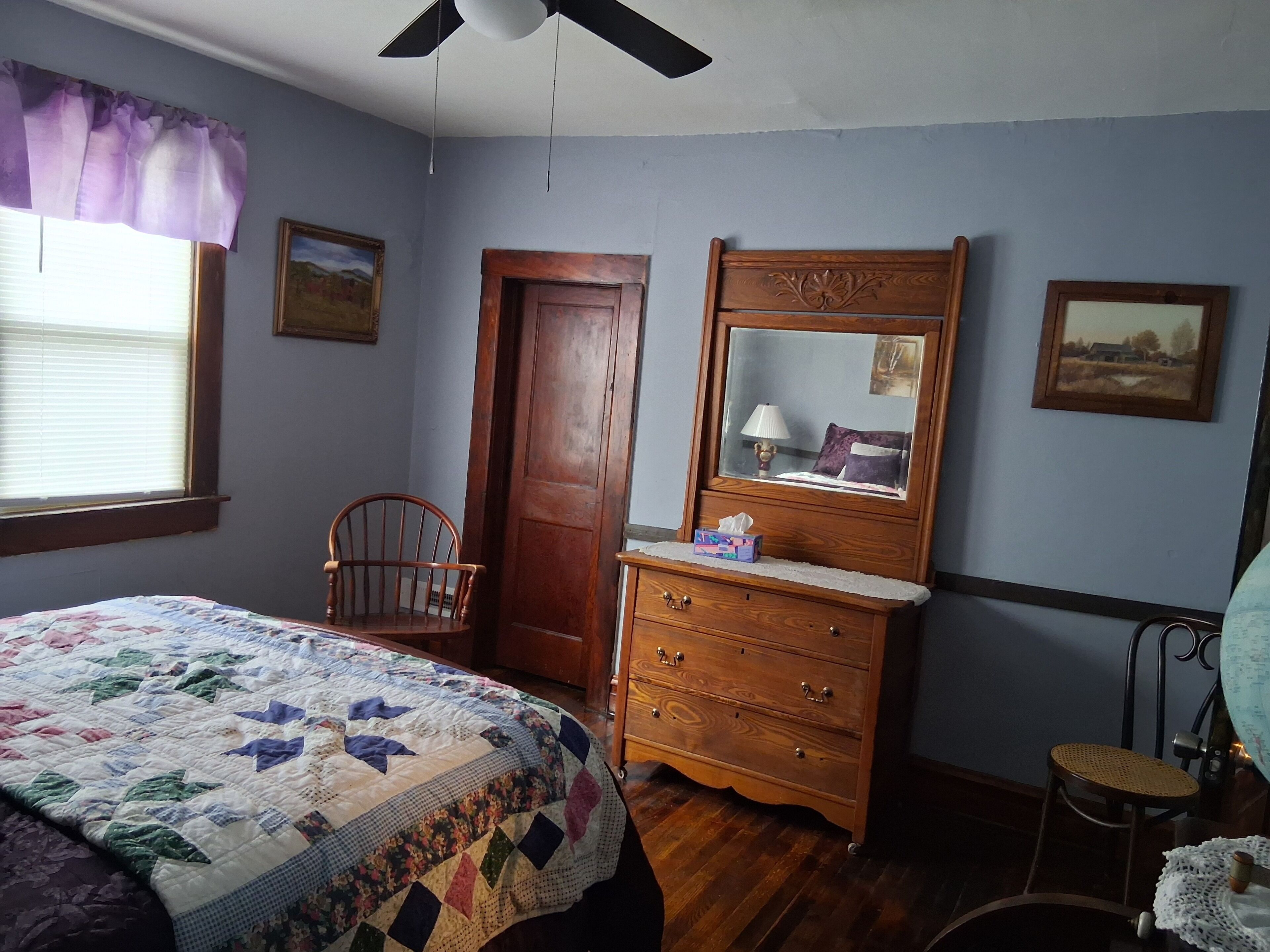 A bedroom with a bed, dresser, chair, and a ceiling fan.
