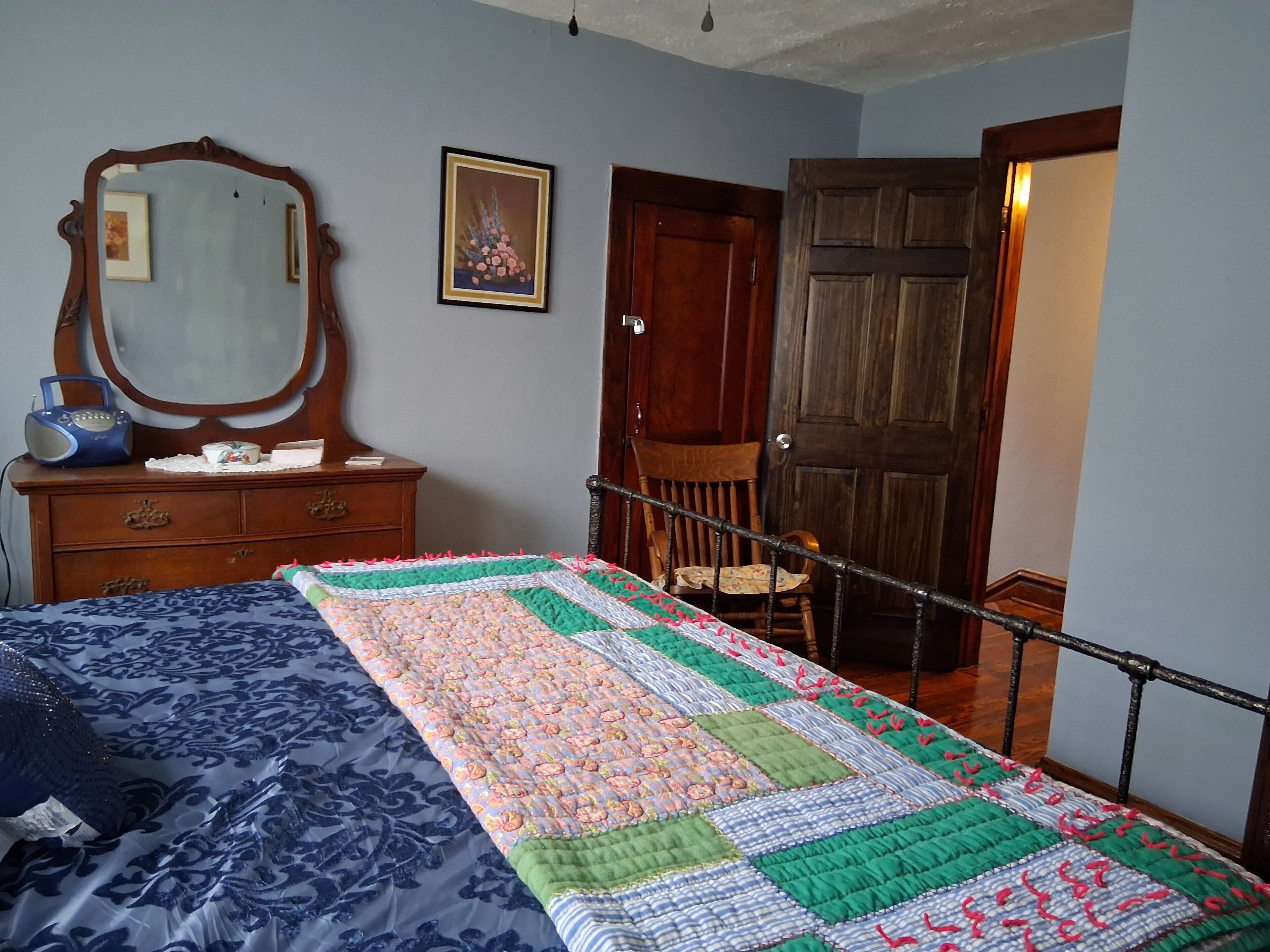 Ein Schlafzimmer mit Bett, Kommode, Spiegel und einer Tür zu einem anderen Raum.