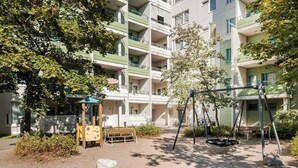A playground with swings and a small playhouse, surrounded by apartment buildings. - Bright 2-bedroom apartment with heating system in beautiful Espoo (Espoo)
