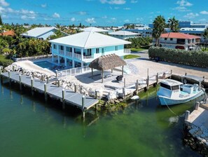 A coastal property with a pool, a boat dock, and a thatched-roof structure. - Dockside Paradise | Brand New, Large Dock, Private Pool, Tiki Hut, Walk to Sombrero Beach (Marathon)