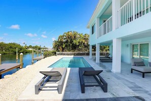 A pool with lounge chairs, a building with a balcony, and a view of the water. - Dockside Paradise | Brand New, Large Dock, Private Pool, Tiki Hut, Walk to Sombrero Beach (Marathon)