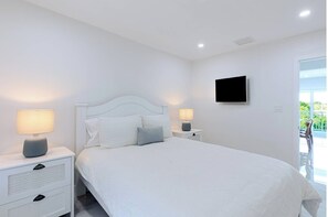 A bedroom with a bed, two bedside tables with lamps, a flat-screen TV, and a window. - Dockside Paradise | Brand New, Large Dock, Private Pool, Tiki Hut, Walk to Sombrero Beach (Marathon)