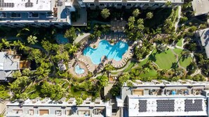 Vista aérea de um resort com vários edifícios, uma piscina central e vegetação ao redor.