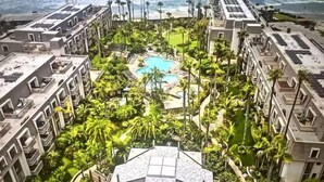 Um hotel moderno com vários sacadões, piscina central e vegetação exuberante.