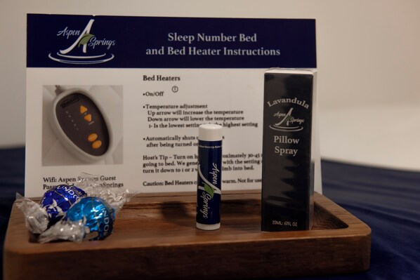 A wooden tray with a lavender-scented pillow spray, a remote control, and two wrapped chocolates.