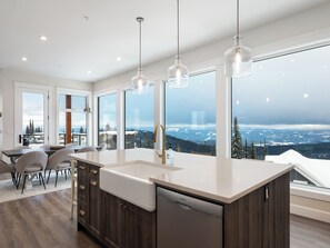 Eine moderne Küche mit einer großen Kochinsel, dunklen Holfschränken und einem Geschirrspüler von Bosch. Große Fenster bieten einen Blick auf eine verschneite Landschaft.