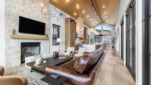 A spacious living area with a stone fireplace, leather sofa, and a modern kitchen in the background. - 2 Min to Jordanelle Gondola Hot Tub Spa Suite Movie Room & Mountain Views Skyridge Summit by Avantstay (Heber City)