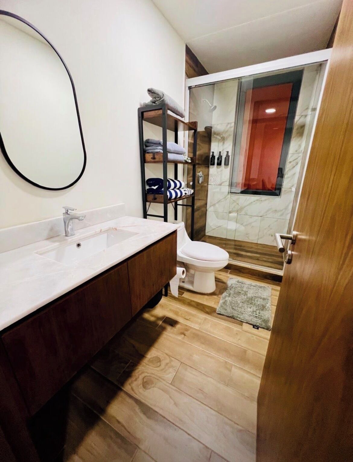 A modern bathroom with a wooden vanity, a toilet, and a glass shower enclosure.