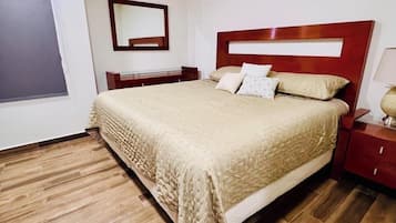 A bedroom with a large bed, wooden flooring, a nightstand, a bedside table, and a mirror on the wall.