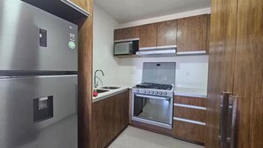 A compact kitchen with a stainless steel refrigerator, a microwave, a stove, and wooden cabinets.