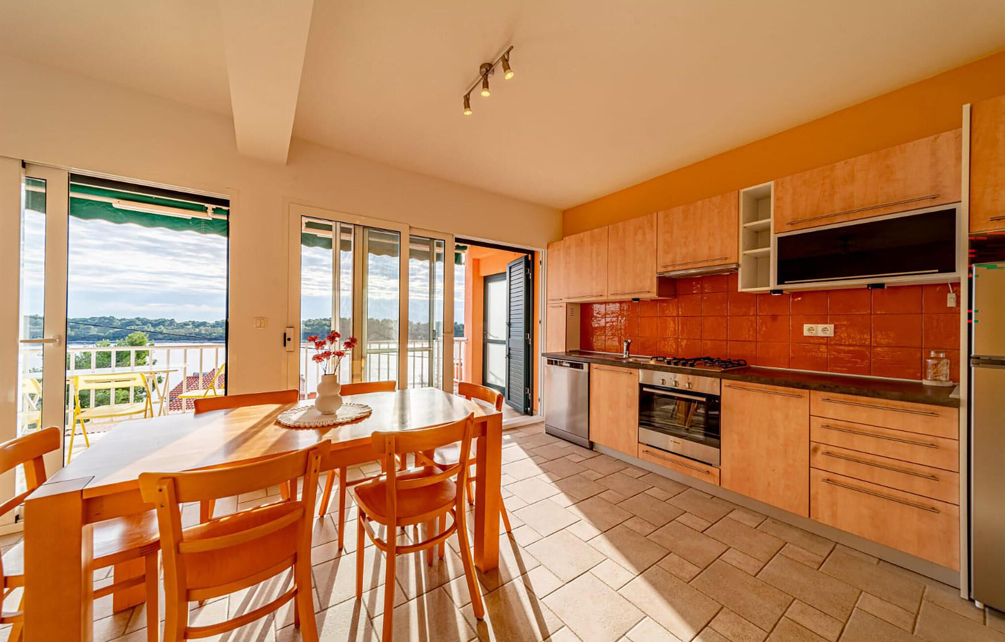A modern kitchen with wooden cabinets, a dining area with a table and chairs, and a view of the outdoors.