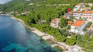 Une zone côtière avec des bâtiments, une mer d’un bleu limpide et une colline boisée.
