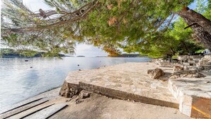 Une zone riveraine pavée de pierres, avec un banc et un arbre qui offrent de l’ombre.