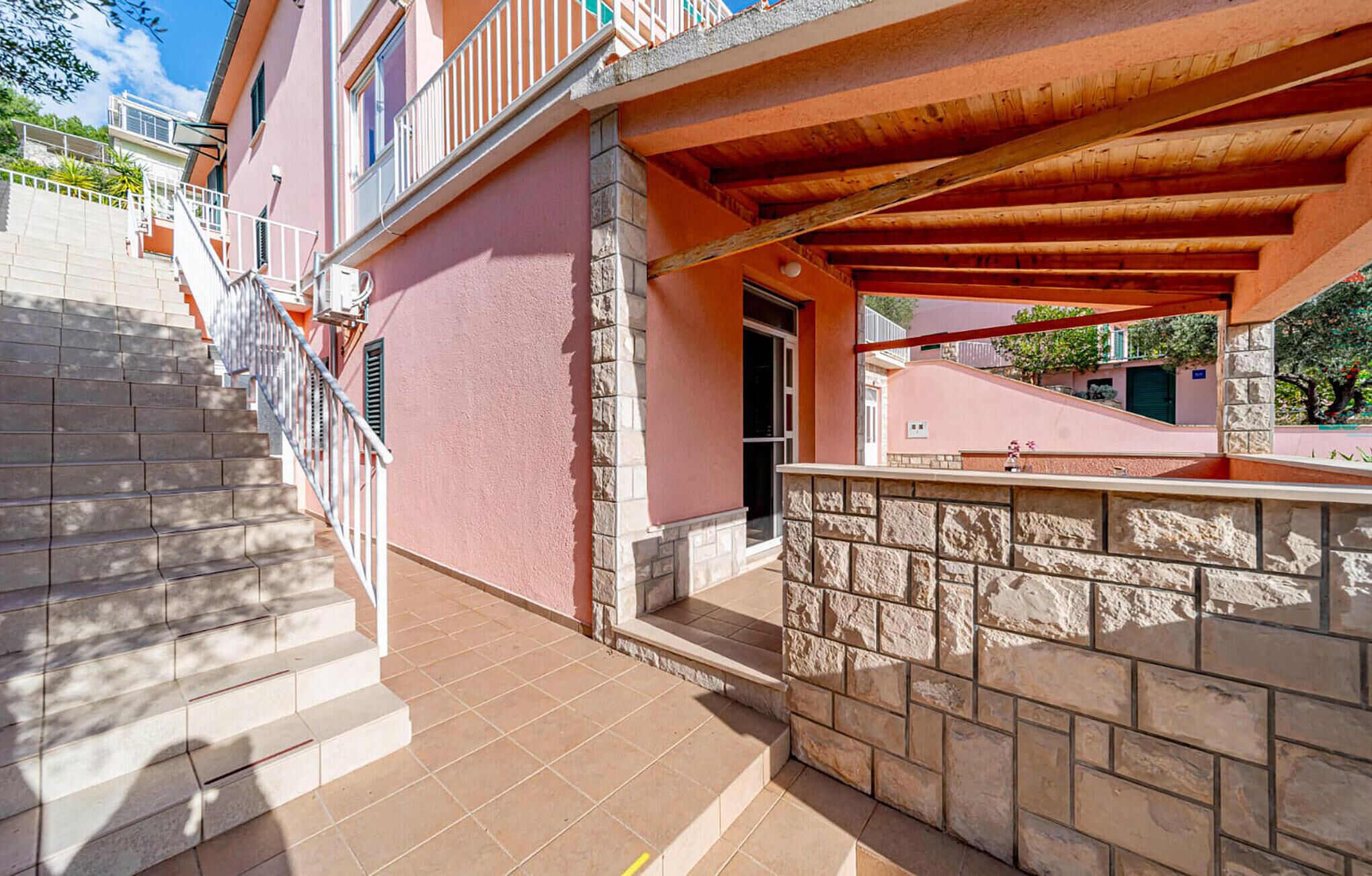 Ein mehrstöckiges Gebäude mit rosa Fassade, Steinstufen und einem überdachten Außenbereich mit Holzboden.