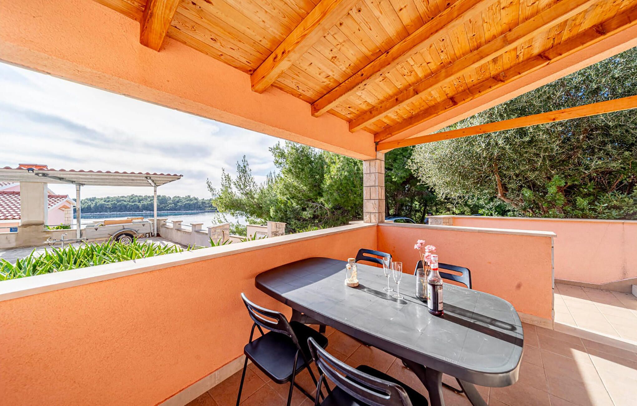 Eine Terrasse im Freien mit Tisch und Stühlen, mit Blick auf ein Gewässer und viel Grün.