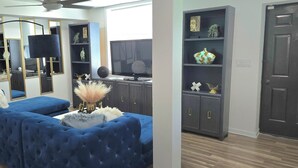 Una sala de estar moderna con un sofá seccional azul, un televisor de pantalla plana y un mueble de madera oscura con objetos decorativos.