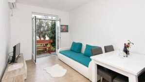 Un soggiorno moderno con un divano bianco, cuscini color petrolio, un tavolino da caffè bianco e una TV su un supporto in legno.
