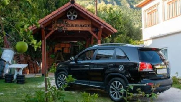 Ein schwarzer SUV vor einem Gebäude mit einem 'GARAGE'-Schild, umgeben von Grünpflanzen und Bergen im Hintergrund.