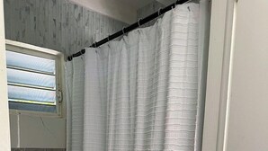 Un baño con inodoro blanco, cortina de ducha y ventana con persianas.