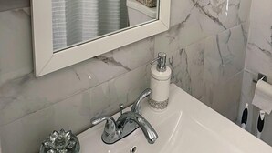 Un baño con lavamanos blanco, espejo y baldosas de mármol.