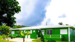 Un edificio verde con techo plano, rodeado de césped y una palmera de plátano.
