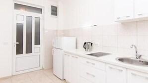 Una cocina pequeña y blanca con un refrigerador, un hervidor y un lavamanos.
