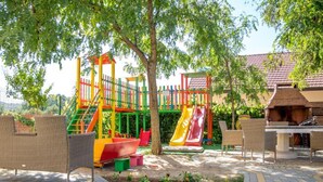 Un parque infantil con toboganes y estructuras para escalar, rodeado de árboles y asientos al aire libre.