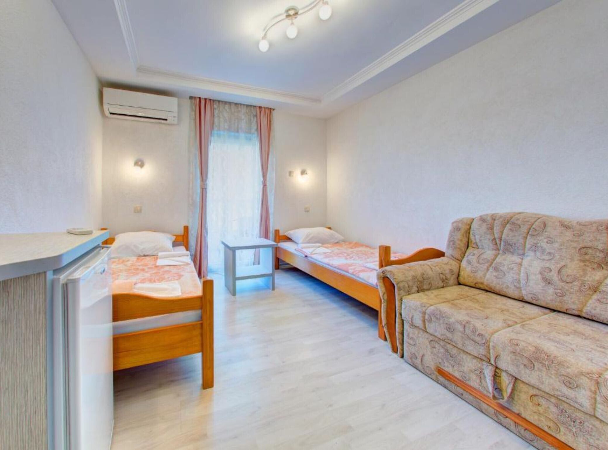 Una habitación pequeña y bien iluminada con dos camas individuales, un sofá, una mesita y un equipo de aire acondicionado.