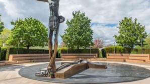 Une statue de Jésus-Christ sur la croix, située dans une place circulaire agrémentée de bancs et d’arbres.