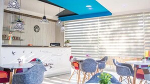 A modern dining area with a white counter, blue ceiling accents, and a large window with blinds.