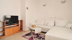 Una sala de estar moderna con un televisor de pantalla plana sobre un mueble de madera, un sofá blanco, una mesita con superficie de vidrio y una alfombra estampada.