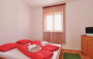 A single bed with red bedding, a television on a wooden cabinet, and a window with curtains. - Amazing apartment in Nin with WiFi (Nin)