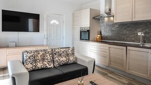 A compact living space with a sofa, a flat-screen TV, a kitchenette with a stove, and a door. - Gorgeous home in Posedarje (Posedarje)