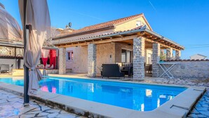 A poolside area with a stone pool, outdoor seating, and a covered patio. - Gorgeous home in Posedarje (Posedarje)
