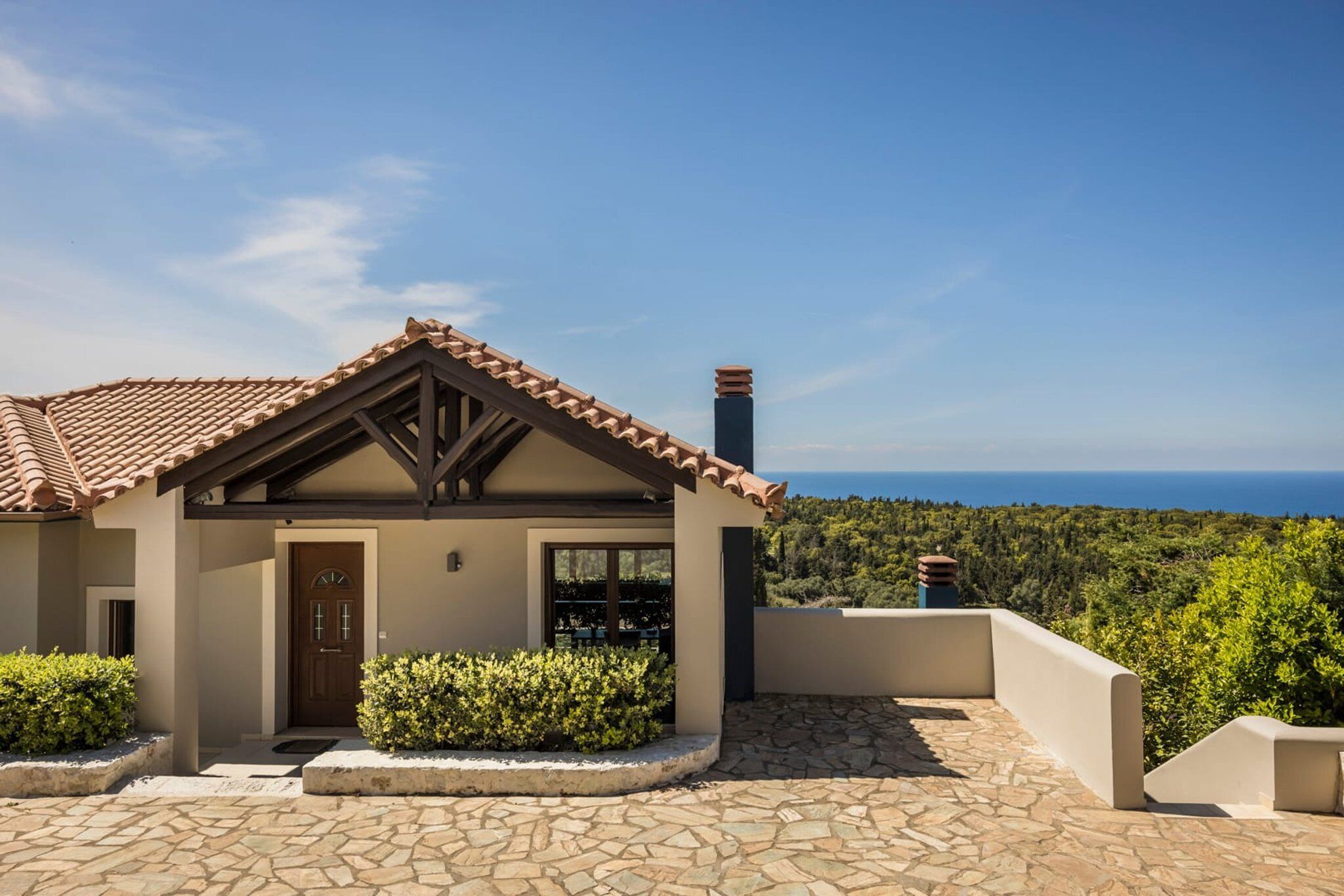 Ein Haus mit einer Steinterrasse, einer Holztür und Blick auf das Meer.