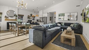 Una sala moderna con un sofá modular, comedor, cocina y un espejo grande.