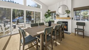 Un comedor amplio con una gran mesa y sillas de madera, chimenea y ventanas que ofrecen vistas a un paisaje nevado.