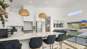 Una cocina moderna con armarios blancos, una isla grande con taburetes de bar, un refrigerador de acero inoxidable y una lámpara colgante de fibra natural.