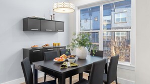 A dining area with a table set for breakfast, a large window with a view of a building, and a black cabinet above the table. - Rooftop Deck w/ Hot Tub Near Dining & Ski Slopes The Lookout by Avantstay (Park City)
