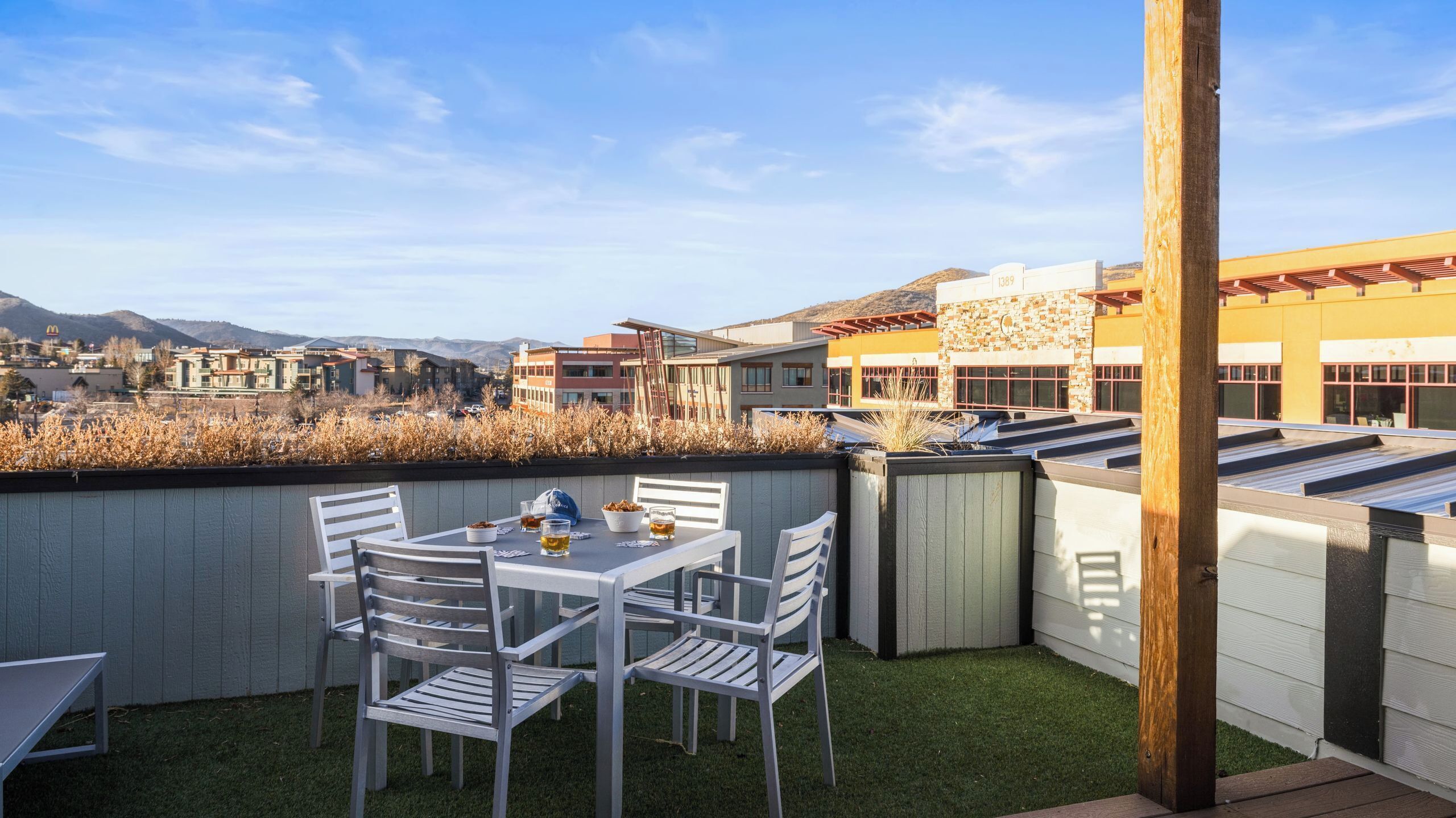 A rooftop patio with a table and chairs, a view of buildings in the background, and a clear sky.