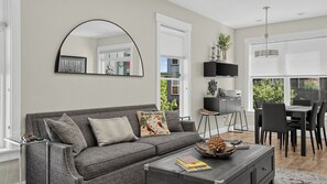 A modern living room with a grey sofa, a coffee table, and a dining area with a table and chairs. - Rooftop Deck w/ Hot Tub Near Dining & Ski Slopes The Lookout by Avantstay (Park City)