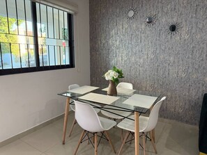 A dining area with a glass table, white chairs, and a vase of flowers. - Rio Nilo Apartments (Mazatlán)
