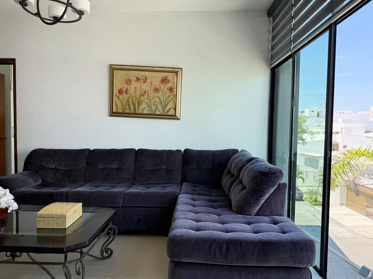 A modern living room with a dark-colored sectional sofa, a glass coffee table, and a framed floral artwork on the wall.