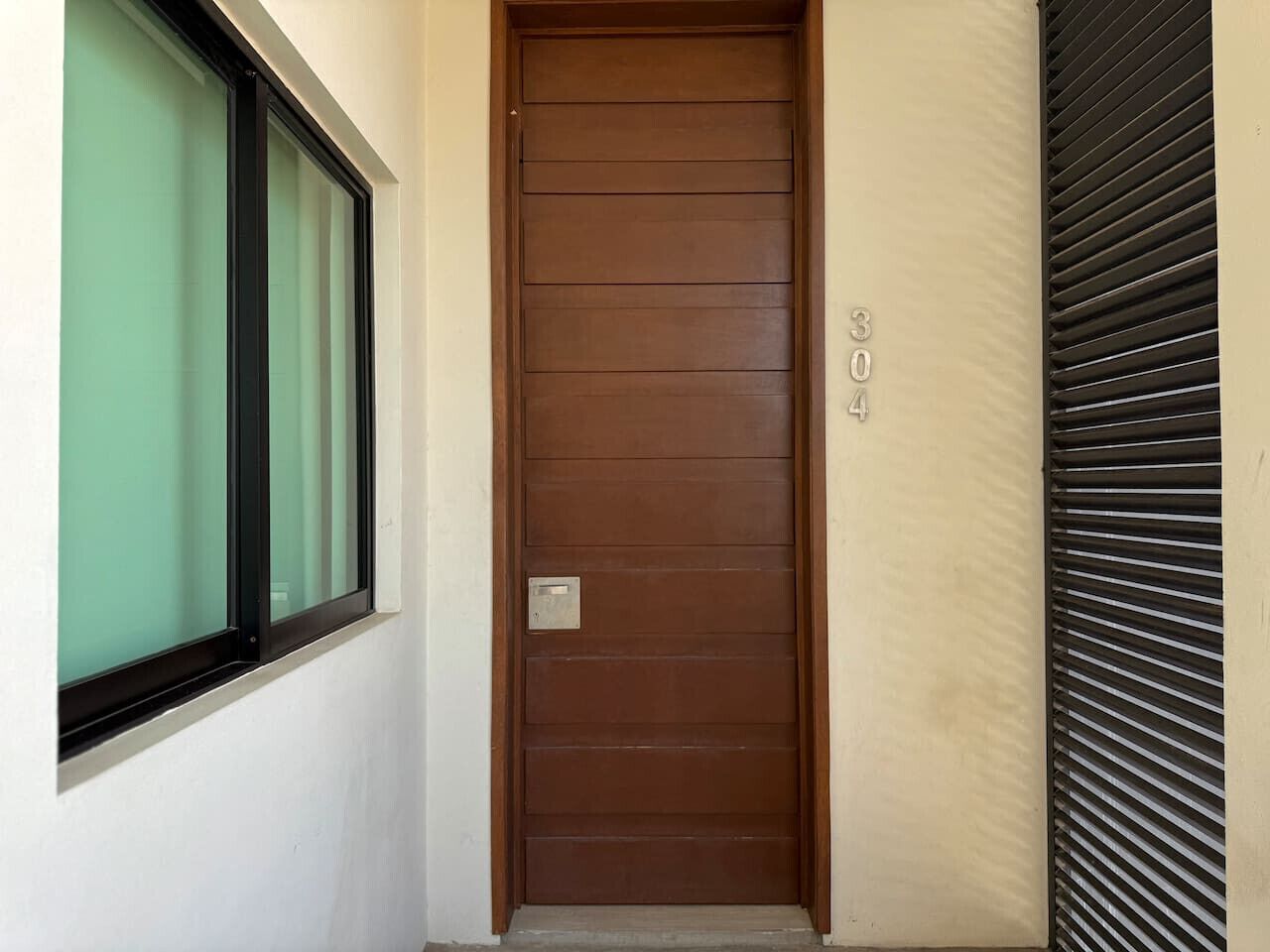 A brown door with a window to the left and a shutter to the right.