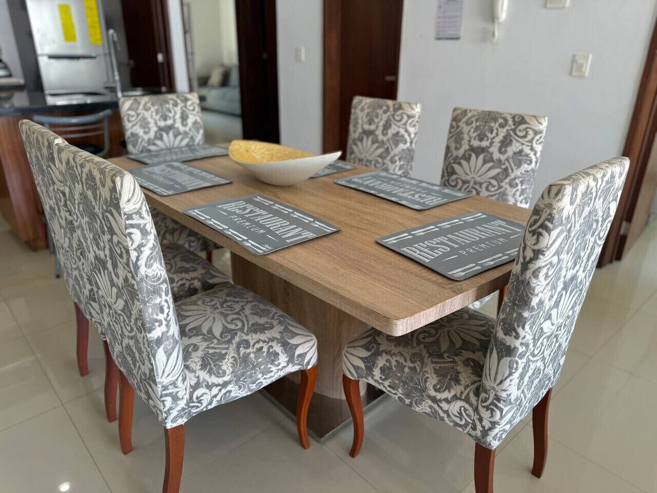 Una mesa de comedor con cuatro sillas, cada una con un cojín estampado. La mesa tiene una superficie de madera y un cuenco central.