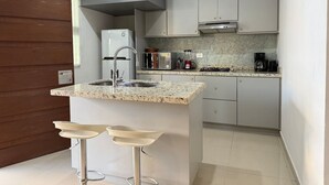 A modern kitchen with a granite countertop, stainless steel appliances, and a built-in island with bar stools. - Rio Nilo Apartments (Mazatlán)