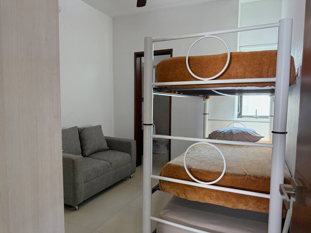 A bunk bed with two levels, a grey sofa, and a window in the background.