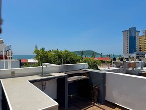 Een terras op het dak met een gootsteen en barbecue, met uitzicht op een stadsbeeld en de zee.