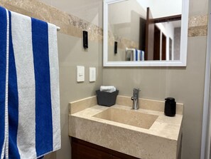 Een badkamer met een beige aanrecht, een wastafel, een spiegel en een handdoek aan een rek.