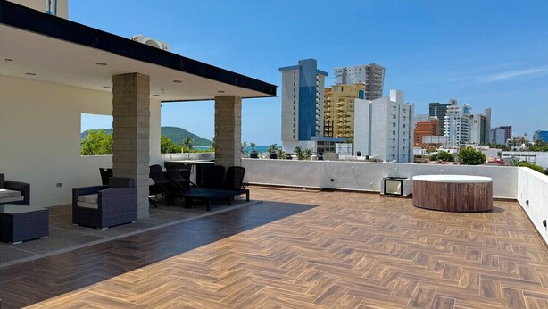A rooftop terrace with outdoor seating, a circular wooden table, and a view of the city skyline. - Rio Nilo Apartments (Mazatlán)